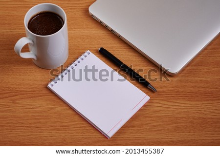 Closed Laptop Beside Empty Journal With Pen And Coffee Mug Over Table. Notebook Computer With Blank Notepad Ballpen Beside Cup Placed Above Work Desk. Royalty-Free Stock Photo #2013455387