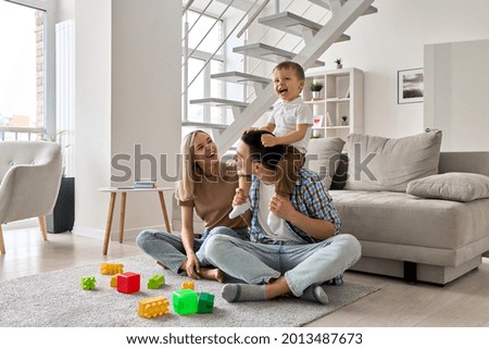 Happy young family couple having fun playing with happy cute kid boy sitting on dads shoulders in modern living room. Parents and toddler child son enjoying spending time sitting on floor at home. Royalty-Free Stock Photo #2013487673