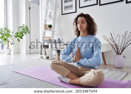 Healthy serene young woman meditating at home with eyes closed doing pilates breathing exercises, relaxing body and mind sitting on floor in living room. Mental health and meditation for no stress. Royalty-Free Stock Photo #2013487694