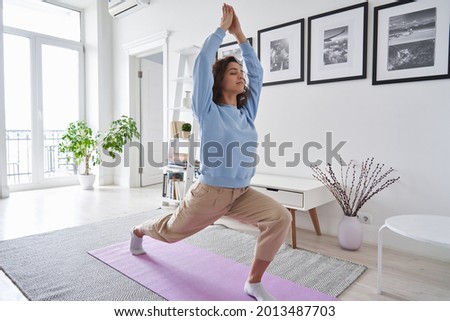 Fit healthy young woman doing pilates yoga exercise fitness training workout at home interior standing in warrior pose. Physical activity for body and mind relaxation, healthy lifestyle habits concept Royalty-Free Stock Photo #2013487703