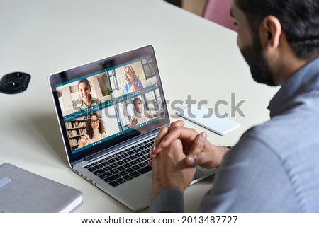 Indian business man having virtual team meeting on video conference call using laptop work from home office talking to diverse people group in remote teamwork online distance chat. Over shoulder view Royalty-Free Stock Photo #2013487727