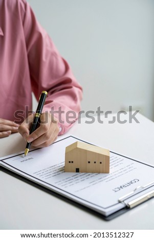 Real estate agent holding home and signing contract about agreement of real property on desk, businessman writing on document form rent house, house broker and planning investment,  business concept