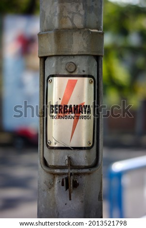An electric pole affixed with a danger sign sticker. (Indonesian for "Danger, high voltage")