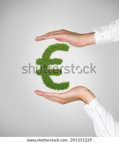 Euro sign which is made of green grass is protected by hands. 