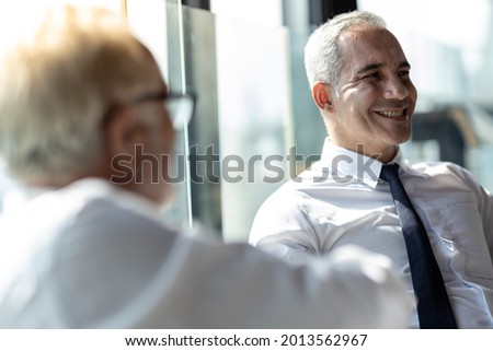 Picture of young business man discussing with his older business partner. They are in white shirt and black tie. They are sitting on a table in a hotel lobby