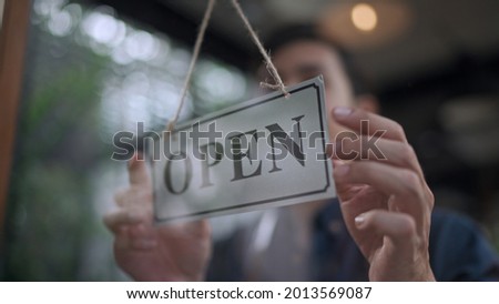 Soft focus, View through window, Close up hand of  Handsome young man owner hanging storefront sign to Opfen at cafe or restaurant, small business service concept