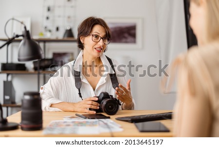 Professional photographer sitting at bright office and talking with client about photo session.Two women discussing working details indoors. Royalty-Free Stock Photo #2013645197