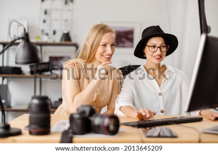 Competent photographer and client reviewing taken pictures on computer at bright office. Two caucasian women choosing photos after photo session.