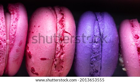 Dark pink and purple macaroons in a box  agains a black background.