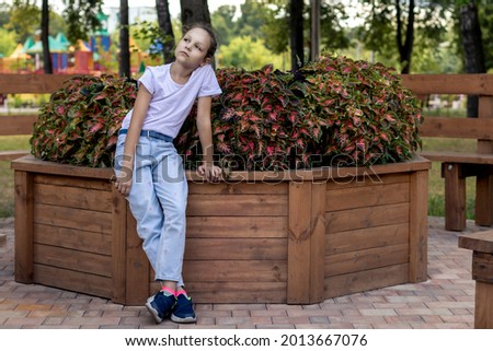 The girl looks into the distance while sitting on a garden flower garden with plants. Portrait of a girl for mock-ups, logos or designer prints with free space on the city streets.