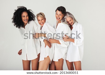 Studio shot of diverse women embracing their natural and aging bodies. Four confident and happy women smiling cheerfully while wearing white shirts against a white background. Royalty-Free Stock Photo #2013680051