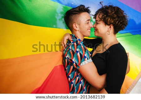 Romantic couple bonding against a rainbow pride flag. Young LGBTQ couple embracing each other and touching their noses together. Two non-conforming lovers smiling while standing together. Royalty-Free Stock Photo #2013682139