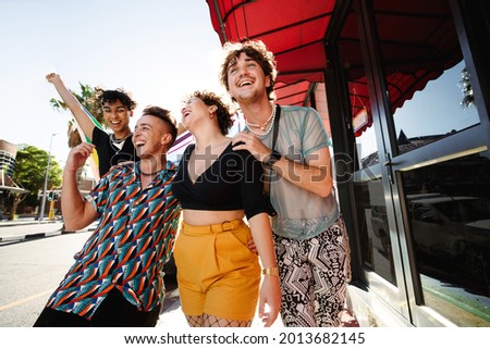 Happy young LGBTQ+ people parading the rainbow pride flag outdoors. Group of non-conforming young people smiling cheerfully while holding the rainbow pride flag. Friends walking together. Royalty-Free Stock Photo #2013682145