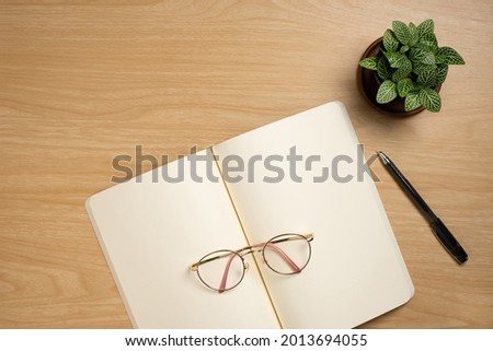 Desk office with blank notepad, flower and pen on wood table. Flat lay top view copy space.