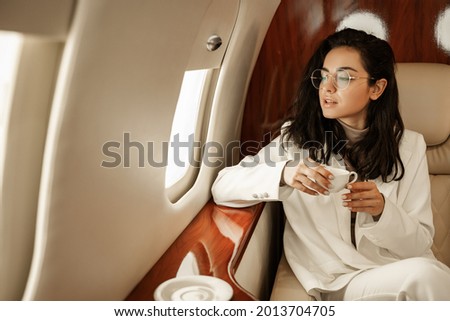 For the first time since quarantine, a young women delegate flies to a business meeting, looking out the window and drinking coffee on board the plane. Travel after covid pandemic Royalty-Free Stock Photo #2013704705