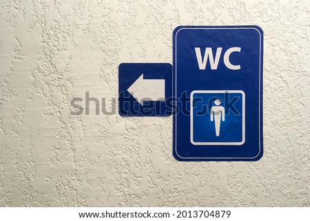 Arrow, pointer on blue plate of public male toilet signÐ± on plastered wall. Toilet sign. Restroom Concept .WC. Horizontal shot. Copy space. Close-up. Indoors.
