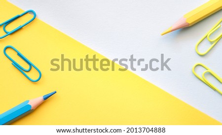 Yellow blue geometric background with yellow and blue pencils and paper clips.
