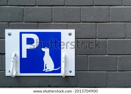 Designated dog parking sign on blue plate. Place for bind dogs waiting for owners outside, with rings for attaching leash, on public place area or shop. Copy space. Close-up. Outdoors.