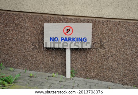 A painted wood signboard on a pole with the inscription no parking next to the building