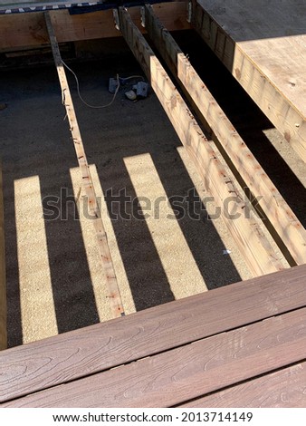 Building a deck in a suburban backyard. The weathered wood foundation is in place and the contractor is laying down composite wood and is halfway through the deck. The railings are demolished.