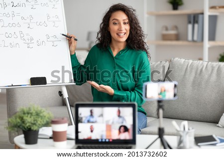Modern Teacher. Smiling Woman Filming Virtual Video Lecture For Educational Blog Sitting In Front Of Laptop And Mobile Camera Indoors. Remote Tutoring And E-Teaching Concept. Live Streaming Royalty-Free Stock Photo #2013732602