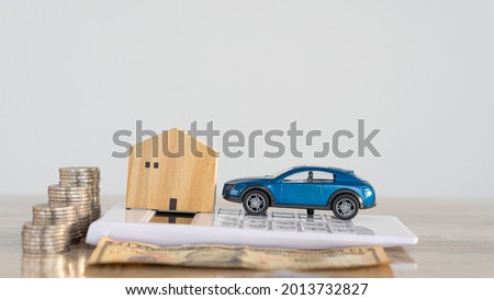 Small wooden house and car on a calculator with piles of coins on the table, car home payment concept.