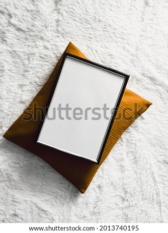 Black thin wooden frame with blank copyspace as poster photo print mockup, golden cushion pillow and fluffy white blanket, flat lay background and art product, top view