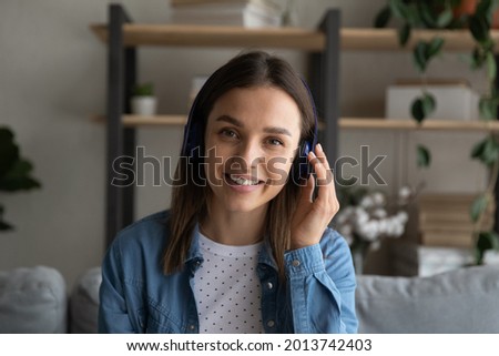 Profile picture attractive woman sit on couch look at camera listens to friend through wireless headphones. Applicant participate in job interview remotely by video call. Virtual meeting event concept Royalty-Free Stock Photo #2013742403