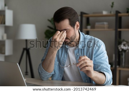 Itchy dry eyes, allergy, need drops concept. Tired overworked businessman sit at desk after laptop usage feeling eyestrain takes off glasses rubbing nose bridge reduce ache of irritated exhausted eyes Royalty-Free Stock Photo #2013742469