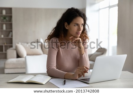 Pensive young Hispanic woman sit at desk at home office work online on laptop thinking pondering. Thoughtful millennial Latino female use computer look in distance make plans or solve problem. Royalty-Free Stock Photo #2013742808