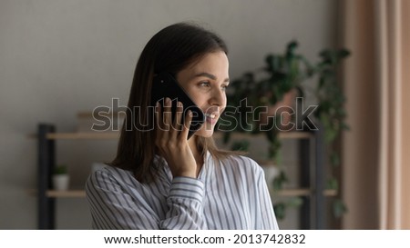 Happy woman standing at home talks on the phone looks out window, having pleasant personal conversation to friend or family remotely using mobile carrier operator, communication, modern tech concept Royalty-Free Stock Photo #2013742832