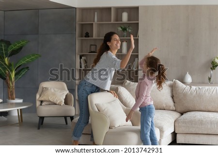 Overjoyed young Latino mother and little teen daughter give high five for well-done house work. Happy Hispanic mom and small teenage girl child celebrate finish job in new home. Rent concept. Royalty-Free Stock Photo #2013742931