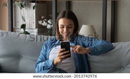 Lovely young woman spend time use smartphone, sit on sofa in living room hold cellphone enjoy chat in social media, search buy goods fashion clothes via e-commerce retail services application concept Royalty-Free Stock Photo #2013742976