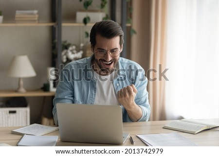 Man sit at desk read e-mail on laptop makes yes gesture feels happy. Male entrepreneur get great business news, celebrate career growth, advance. Achievement, win, moment of auction victory concept Royalty-Free Stock Photo #2013742979