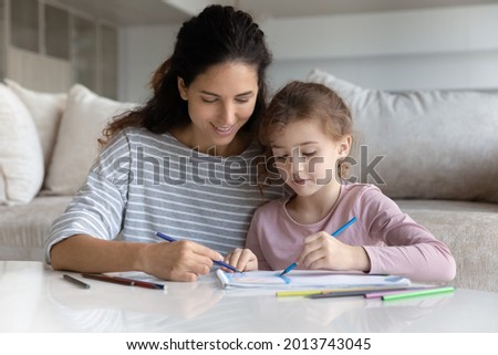 Smiling loving Hispanic mother and small teen biracial daughter have fun drawing painting together. Happy caring Latino mom and little teenage girl child relax engaged in art activity. Hobby concept.