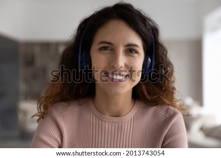 Headshot portrait of smiling young Hispanic woman in headphones talk speak on video call with client customer. Profile picture of happy Latino female in wireless earphones have webcam event.