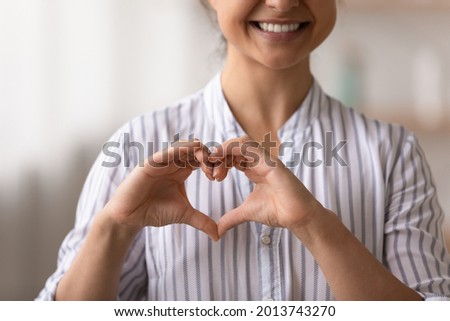 Close up cropped of smiling Indian woman showing heart shape gesture on chest, feeling grateful thankful, happy romantic young female expressing love and care, volunteer supporting patients Royalty-Free Stock Photo #2013743270