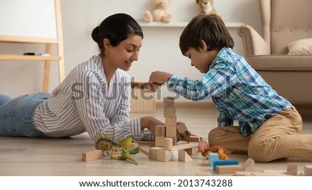 Smiling loving Indian mother and little son playing with toys together, lying on warm wooden floor with underfloor heat, happy young mom and preschool kid having fun at home, building from blocks Royalty-Free Stock Photo #2013743288