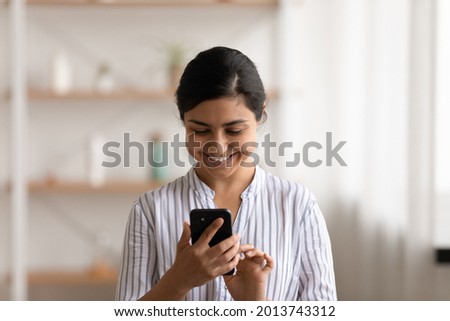 Head shot smiling Indian woman using smartphone, having fun with device, standing at home, positive attractive young female typing writing message in social network, chatting or shopping online Royalty-Free Stock Photo #2013743312