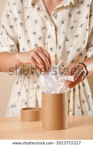 Female hands opening a cylinder packaging made of recycled paper standing on a yellow surface