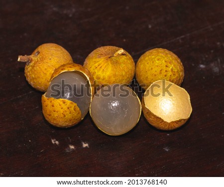 Bunch of longan fruit with brown skin and white flesh isolated on dark brown background with space for text.