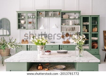 Spacious kitchen with vintage design, counter with marble top and flowers in metal bucket on it, organized furniture with various crockery, comfortable apartment interior Royalty-Free Stock Photo #2013781772