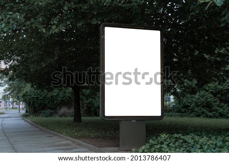 Advertising billboard panel for a mockup. Blank template for ads at a park with green trees. Space for an advertisement billboard at a park. White ad.