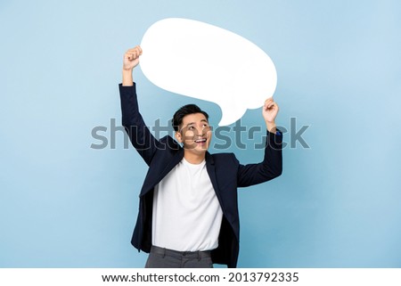 Young happy handsome smiling Asian man holding empty speech bubble in light blue isolated studio background