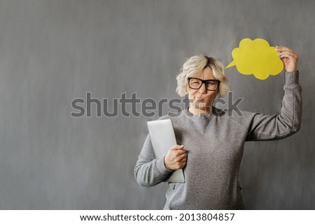 attractive young blonde woman in glasses with laptop in hand and the yellow paper cloud of thoughts on a grey background, model plus size