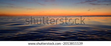 Baltic sea after the rain. Dramatic sunset sky, glowing pink and golden clouds, symmetry reflections in the water. Abstract natural pattern, texture, background. Picturesque panoramic scenery