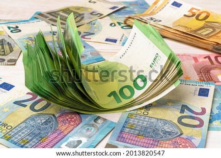 Wad of 100 euro banknotes over euro paper currency background. Concepts of accounting of income and expenses, cash savings, counting money and wealth. Close-up. Front view.