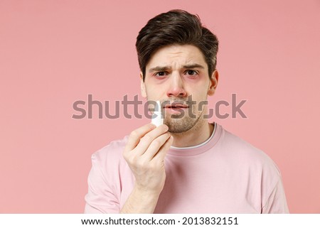 Sick unhealthy ill allergic man has red watery eyes runny stuffy sore nose suffer from allergy symptoms hay fever hold bottle uses instill nasal drops isolated on pastel pink color background studio