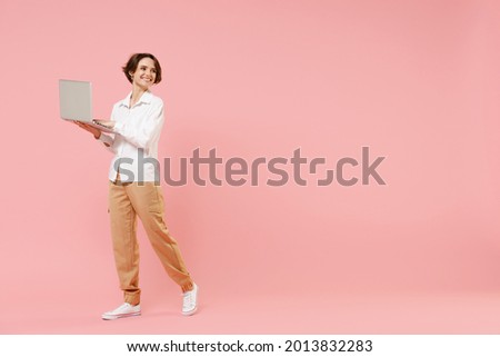 Full length smiling happy young employee business woman corporate lawyer in classic white shirt work in office hold laptop pc computer chat online look aside walk isolated on pastel pink background.