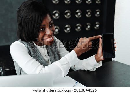Happy african american woman holding a phone in her hands advertising it to her girl